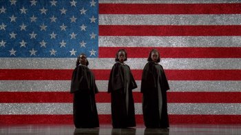 Movie still from “Little Shop of Horrors” (1986), directed by Frank Oz – A group of people standing next to each other in front of an american flag; Extreme Wide shot, Overhead angle