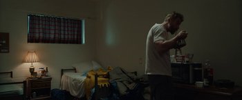 Movie still from “Little Woods” (2018), directed by Nia DaCosta – A man standing in a room next to an unmade bed; Medium shot, Low angle