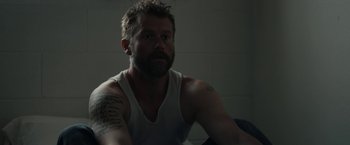 Movie still from “Little Woods” (2018), directed by Nia DaCosta – A man sitting in a room with a beard and a white tank top on; Close Up shot, High angle