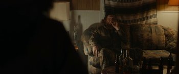 Movie still from “Little Woods” (2018), directed by Nia DaCosta – A man sitting in a chair smoking a cigarette; Medium shot, Over the shoulder angle