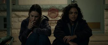 Movie still from “Little Woods” (2018), directed by Nia DaCosta – Two women sitting on the ground smoking a cigarette; Medium shot, Over the shoulder angle