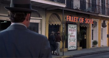 Movie still from “Live and Let Die” (1973), directed by Guy Hamilton – Two men walking down the street in front of a restaurant; Wide shot, Over the shoulder angle