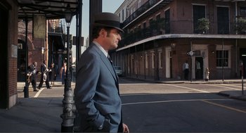 Movie still from “Live and Let Die” (1973), directed by Guy Hamilton – A man wearing a suit and hat standing on a street corner; Wide shot, Low angle