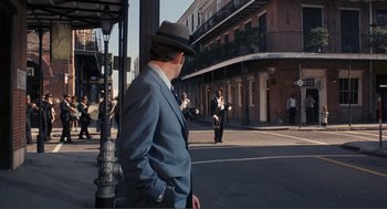 Movie still from “Live and Let Die” (1973), directed by Guy Hamilton – A man wearing a suit and hat standing on a street corner; Extreme Wide shot, Over the shoulder angle