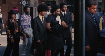 Movie still from “Live and Let Die” (1973), directed by Guy Hamilton – A group of young men standing next to each other on the street; Medium shot, Low angle