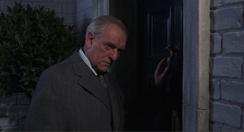 Movie still from “Live and Let Die” (1973), directed by Guy Hamilton – An older man in a suit and tie standing in front of an open door; Close Up shot, Over the shoulder angle