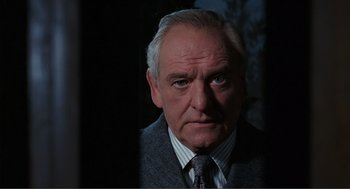 Movie still from “Live and Let Die” (1973), directed by Guy Hamilton – An older man wearing a suit and tie in the dark; Close Up shot, Low angle
