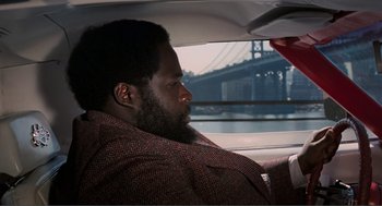 Movie still from “Live and Let Die” (1973), directed by Guy Hamilton – A man sitting in the back seat of a car looking out the window; Close Up shot, Over the shoulder angle