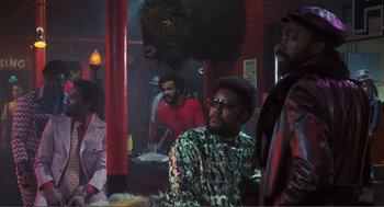 Movie still from “Live and Let Die” (1973), directed by Guy Hamilton – A group of people sitting at a table in a room; Wide shot, Low angle