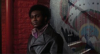 Movie still from “Live and Let Die” (1973), directed by Guy Hamilton – A man wearing a leather jacket standing in front of a brick wall; Medium shot, Low angle