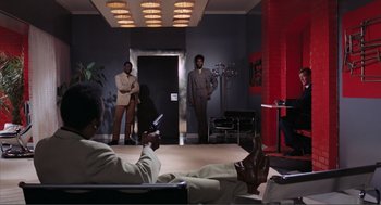 Movie still from “Live and Let Die” (1973), directed by Guy Hamilton – A group of men in suits and ties in a room; Wide shot, High angle