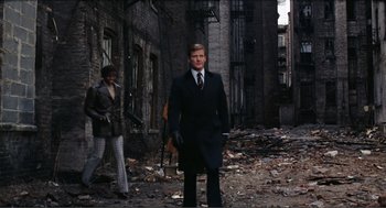 Movie still from “Live and Let Die” (1973), directed by Guy Hamilton – A man wearing a suit and tie standing in a city; Wide shot, Low angle