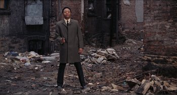 Movie still from “Live and Let Die” (1973), directed by Guy Hamilton – A man standing in the middle of a rubble filled area; Wide shot, Low angle