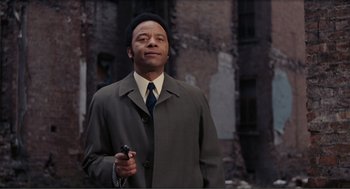 Movie still from “Live and Let Die” (1973), directed by Guy Hamilton – A man in a suit and tie holding a gun; Medium shot, Low angle