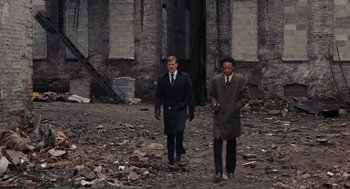Movie still from “Live and Let Die” (1973), directed by Guy Hamilton – Two men in suits and ties walking through a rubble filled area; Wide shot, Low angle
