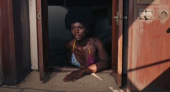 Movie still from “Live and Let Die” (1973), directed by Guy Hamilton – A woman in a bathing suit sitting on the floor; Medium shot, High angle