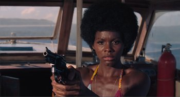 Movie still from “Live and Let Die” (1973), directed by Guy Hamilton – A woman holding a gun while standing in front of a window; Close Up shot, Low angle