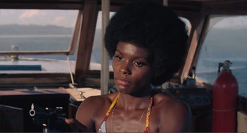 Movie still from “Live and Let Die” (1973), directed by Guy Hamilton – A woman with a large afro sitting on a boat; Close Up shot, Low angle