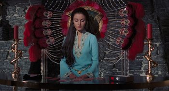 Movie still from “Live and Let Die” (1973), directed by Guy Hamilton – A woman in a blue dress sitting in front of an ornate backdrop; Medium shot, Low angle