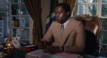 Movie still from “Live and Let Die” (1973), directed by Guy Hamilton – A man wearing a suit and tie writing on a piece of paper; Medium shot, Low angle