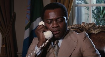 Movie still from “Live and Let Die” (1973), directed by Guy Hamilton – A man talking on a white phone while wearing a suit and tie; Close Up shot, Low angle