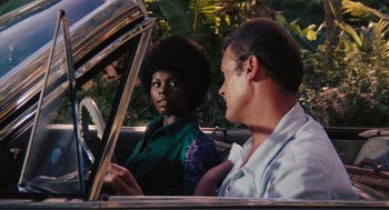 Movie still from “Live and Let Die” (1973), directed by Guy Hamilton – A man and a woman sitting in the back of a car; Medium shot, Over the shoulder angle