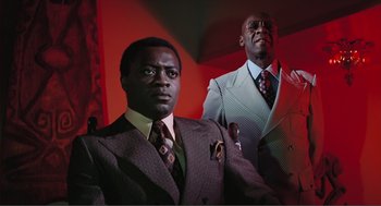 Movie still from “Live and Let Die” (1973), directed by Guy Hamilton – Two men in suits are posing for a picture; Medium shot, Low angle