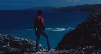 Movie still from “Live and Let Die” (1973), directed by Guy Hamilton – A man standing on top of a hill looking at the ocean; Extreme Wide shot, Low angle