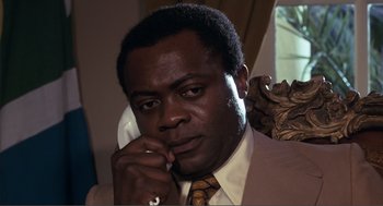 Movie still from “Live and Let Die” (1973), directed by Guy Hamilton – A man in a suit and tie talking on a phone; Close Up shot, Low angle