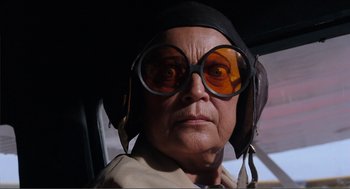 Movie still from “Live and Let Die” (1973), directed by Guy Hamilton – An older woman wearing glasses and wearing a hat; Close Up shot, Low angle