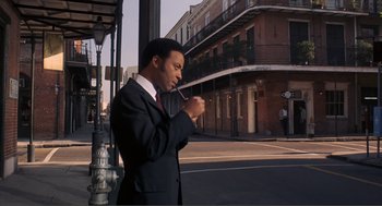 Movie still from “Live and Let Die” (1973), directed by Guy Hamilton – A man in a suit smoking a pipe on a street corner; Medium shot, Low angle