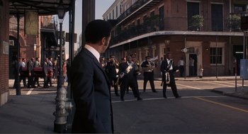 Movie still from “Live and Let Die” (1973), directed by Guy Hamilton – A group of people marching down a street; Extreme Wide shot, Over the shoulder angle