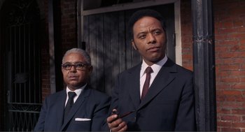 Movie still from “Live and Let Die” (1973), directed by Guy Hamilton – A couple of men standing next to each other in suits; Close Up shot, Low angle