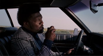 Movie still from “Live and Let Die” (1973), directed by Guy Hamilton – A man sitting in the driver's seat of a car; Medium shot, Low angle