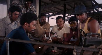 Movie still from “Live and Let Die” (1973), directed by Guy Hamilton – A group of men sitting around a table looking at their cell phones; Medium shot, High angle