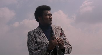 Movie still from “Live and Let Die” (1973), directed by Guy Hamilton – A man in a jacket holding a cell phone in his hands; Medium shot, Low angle