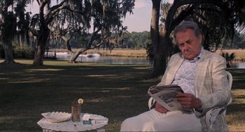 Movie still from “Live and Let Die” (1973), directed by Guy Hamilton – An older man sitting on the grass reading a newspaper; Medium shot, Over the shoulder angle