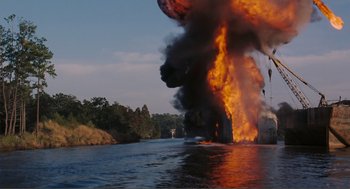 Movie still from “Live and Let Die” (1973), directed by Guy Hamilton – A large fire is burning in the middle of a river; Extreme Wide shot, Low angle