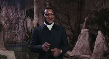 Movie still from “Live and Let Die” (1973), directed by Guy Hamilton – A man wearing a black suit and white shirt; Medium shot, Low angle