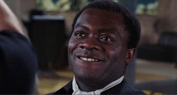 Movie still from “Live and Let Die” (1973), directed by Guy Hamilton – A person wearing a suit and smiling; Close Up shot, High angle