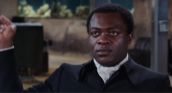 Movie still from “Live and Let Die” (1973), directed by Guy Hamilton – A person wearing a suit and tie; Close Up shot, High angle