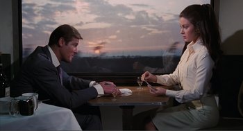 Movie still from “Live and Let Die” (1973), directed by Guy Hamilton – A man and a woman sitting at a dinner table; Medium shot, Over the shoulder angle