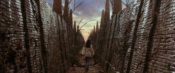 Movie still from “Labyrinth” (1986), directed by Jim Henson – A woman is walking down a path through a chain link fence; Wide shot, Low angle