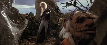 Movie still from “Labyrinth” (1986), directed by Jim Henson – A woman with a long blonde wig standing next to a troll; Medium shot, Over the shoulder angle