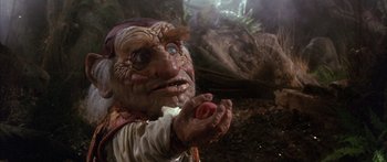 Movie still from “Labyrinth” (1986), directed by Jim Henson – An evil looking creature holding a red apple; Close Up shot, High angle