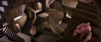 Movie still from “Labyrinth” (1986), directed by Jim Henson – A man standing in a room with many stairs; Extreme Wide shot, Overhead angle