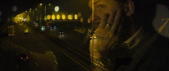 Movie still from “Locke” (2013), directed by Steven Knight – A man with his hand on his face looking out a window at night; Wide shot, Over the shoulder angle