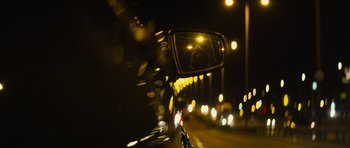 Movie still from “Locke” (2013), directed by Steven Knight – A view of the side view mirror of a car at night; Extreme Wide shot, Over the shoulder angle