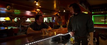 Movie still from “Logan Lucky” (2017), directed by Steven Soderbergh – Two men sitting at a bar talking to each other; Medium shot, Over the shoulder angle