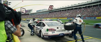 Movie still from “Logan Lucky” (2017), directed by Steven Soderbergh – A group of people standing around a race car; Wide shot, Over the shoulder angle